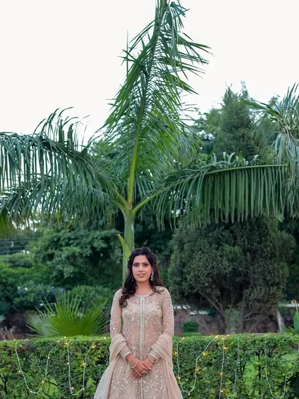 A full-length portrait of the bride-to-be in a lush garden. The natural light and greenery complement her elegant gown.