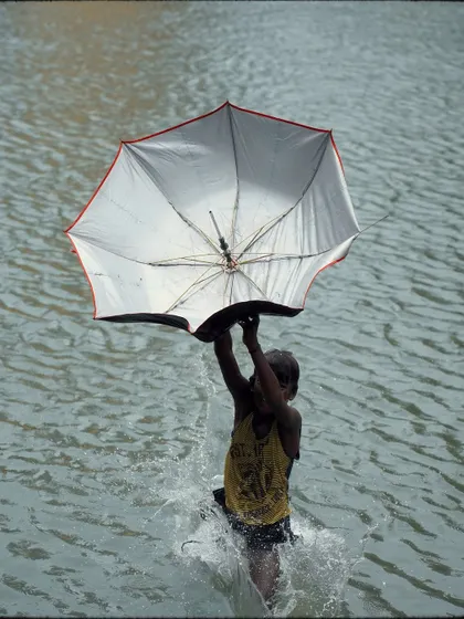 A child uses an umbrella almost like a parachute while jumping into the water, a playful and unique monsoon memory captured at Banganga.