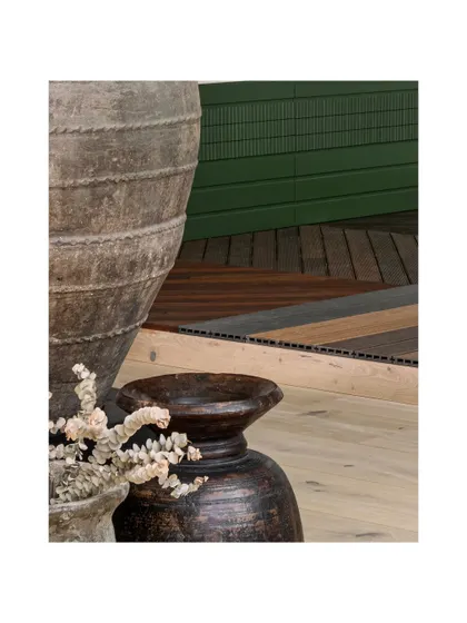 A close-up on the material transition, where rustic urns meet varied wood flooring and a rich green paneled wall. This layering of textures and colors is fundamental to our design approach.