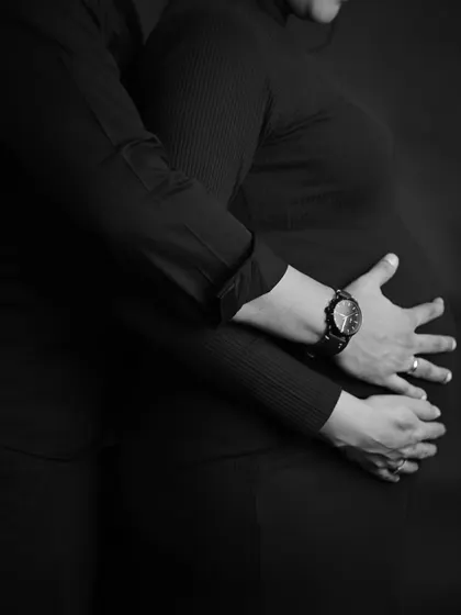 An artistic close-up in black and white, focusing on the hands embracing the baby bump.