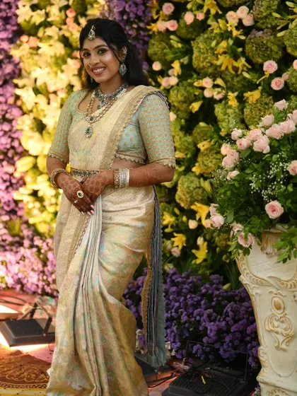 A full-length view of the bride in her pastel green and off-white Kanchivaram ensemble, standing against a beautiful floral backdrop.