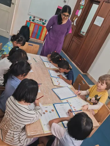 This image shows a focused group of pre-kindergarteners practicing their writing skills. I provide gentle guidance and support as they learn to hold a pencil and form shapes.
