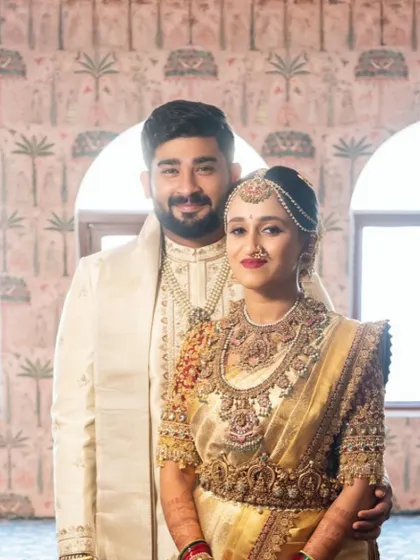 A radiant bride and groom, perfectly coordinated. Her gleaming gold saree with a rich red blouse is complemented by his elegant off white sherwani, showcasing my work in creating harmonious couple attire.