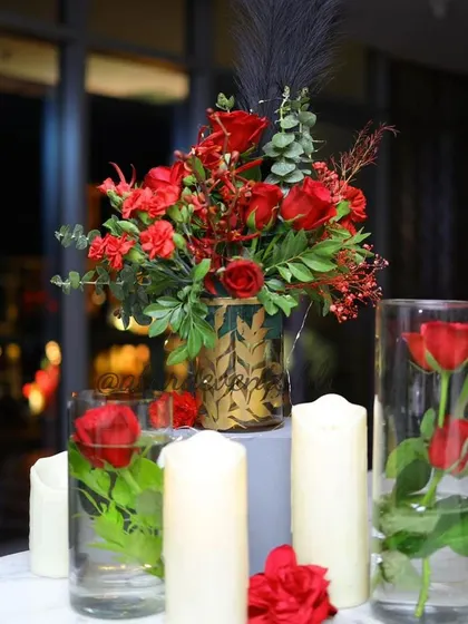 A centerpiece dettaglio from a 40th birthday party. Red roses are arranged in a gold-patterned vase and surrounded by candles, creating a rich and elegant tablescape.
