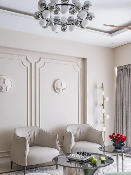 A pair of sophisticated off-white armchairs sit opposite a black marble coffee table, set against a wall with classic molding. The design is clean, modern, and timeless.