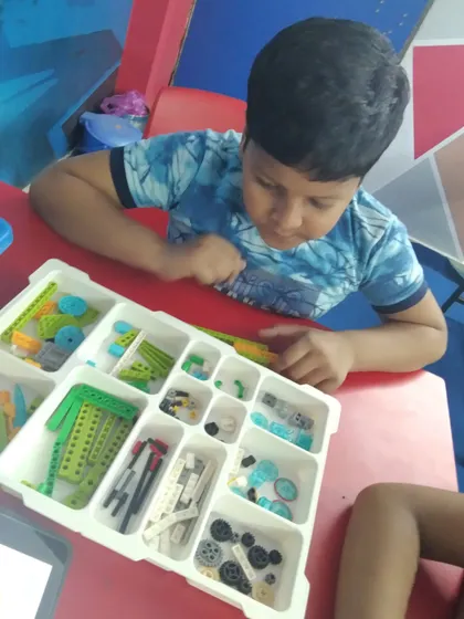 A student carefully selects components from a robotics kit, a key part of the planning and building process in our project-based sessions.