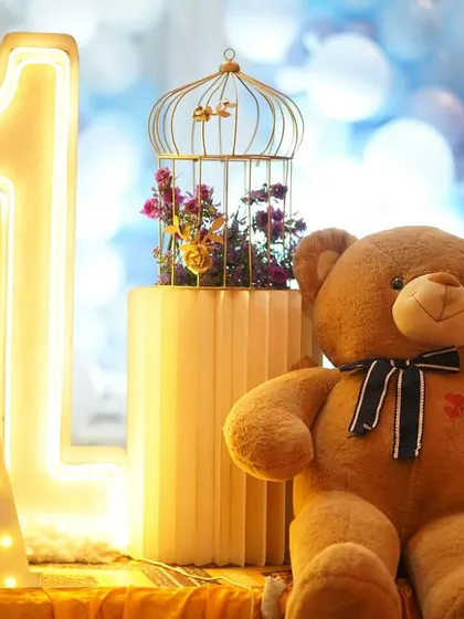 A close-up of a teddy bear themed decor, showing the large neon number '1' next to a cute teddy bear and a birdcage prop with flowers inside.