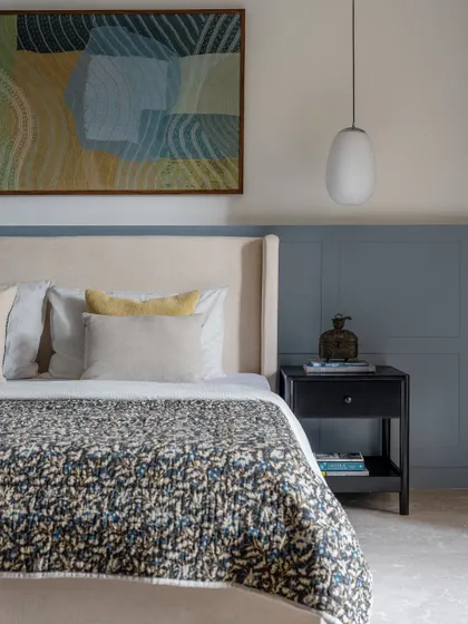 This bedroom showcases a calm and understated design. We used a soft blue-grey on the paneled wall as a backdrop for the upholstered bed and abstract art, creating a serene and restful atmosphere.