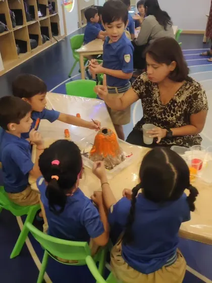 An instructor guides a small group of students at a school workshop as they create a chemical reaction in their model volcano.