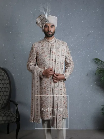 A silhouette of nobility, this coffee beige sherwani blooms with embellished floral artistry and jeweled beadwork. The lace-wrapped safa crowned with a sarpech completes its princely aura.