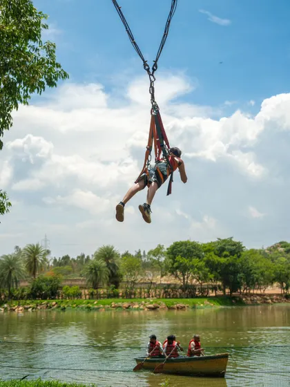 A participant flies through the air on the Superman Swing, with the lake and boats visible below.