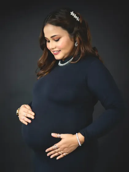 A classic three-quarter portrait of a mom-to-be cradling her bump. The simple dark dress and background keep the focus on her happy and peaceful expression.