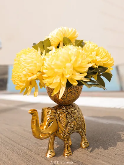 We incorporate symbolic and decorative elements into our designs, like this small golden elephant figurine holding a bouquet of bright yellow chrysanthemums. This piece is perfect for adding a traditional and auspicious touch to a Haldi ceremony.