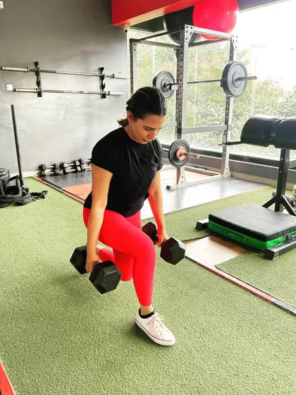 A client performs dumbbell lunges in bright red leggings, adding a vibrant energy to her workout.