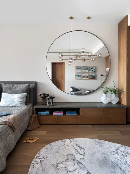 The guest bedroom in the DLF Camellias apartment features a large circular mirror that acts as a stunning focal point. It reflects a custom sculptural light fixture, doubling the impact and adding a sense of drama and sophistication to the room.