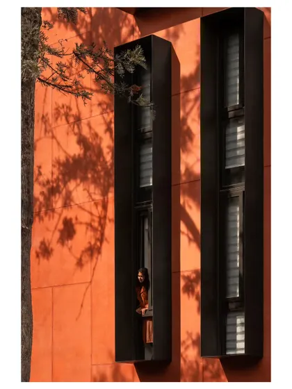 A person looks out from one of the deep-set windows, illustrating the connection between the interior workspace and the natural environment outside. The design fosters moments of quiet reflection.