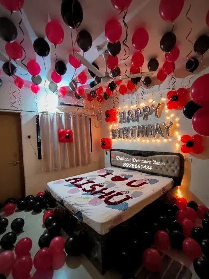 A romantic red and black themed birthday room decoration. The setup includes balloons on the ceiling and floor, and a personalized message on the bed.