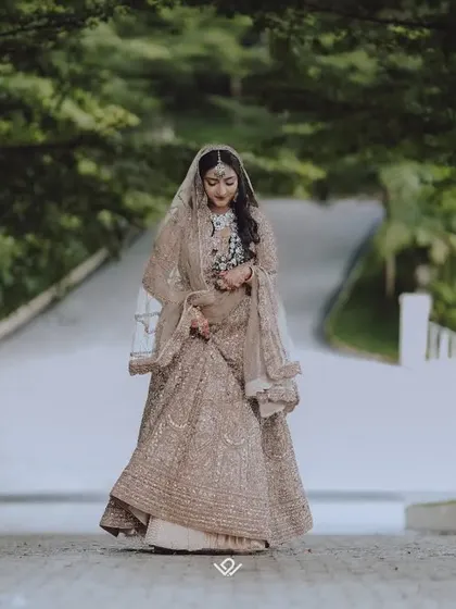A full-length shot of a Muslim bride walking down a tree-lined path, her elegant lehenga flowing.