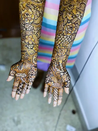 A full view of a bridal henna design with intricate patterns covering both arms.