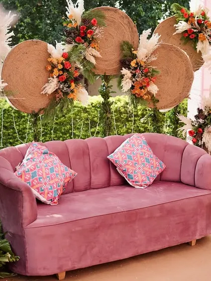 A close-up of the bride's seating for the boho-chic Mehendi, featuring a dusty pink sofa set against a backdrop of woven mats and dried floral arrangements.