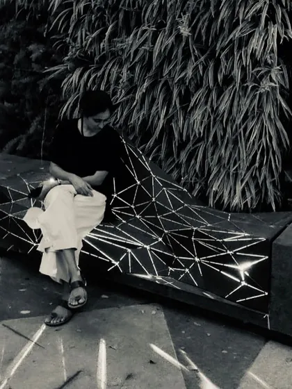 A black and white photo of the architect sitting on the illuminated "Origami" bench. The image captures a quiet moment, showcasing the bench as both a functional object and a piece of light art.