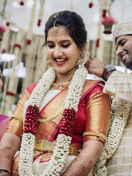 The groom places the sacred necklace on his bride, a pivotal moment in their ceremony. The bride's happy smile and the presence of her mother make this a heartwarming and significant photograph.