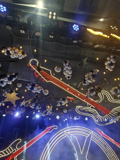 A stunning view of a rock-and-roll themed ceiling. The space is filled with neon guitars, balloon clouds, and spotlights, creating an electrifying atmosphere perfect for a music festival-style party.