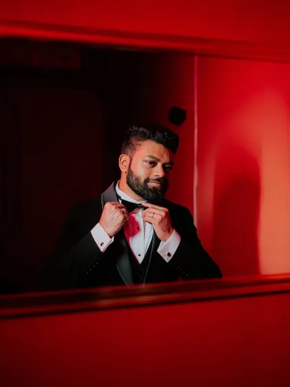 The groom adjusts his bow tie in the mirror, a classic getting-ready portrait.
