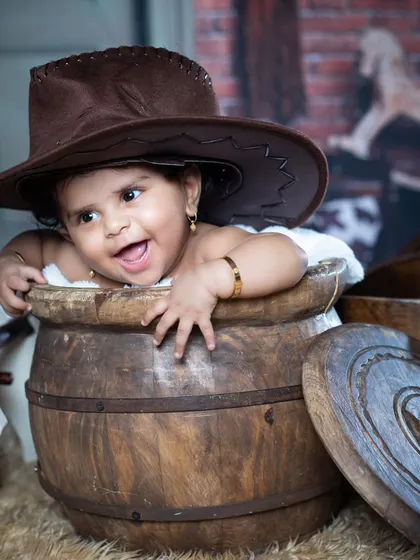 This little cowgirl is peeking out of a barrel, with a big, happy smile.