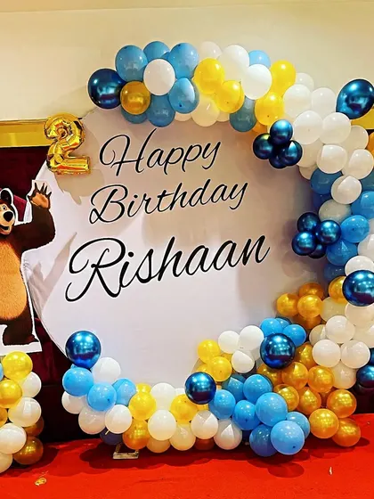 A Masha and the Bear themed second birthday with a circular backdrop and a blue, white, and yellow balloon arch.