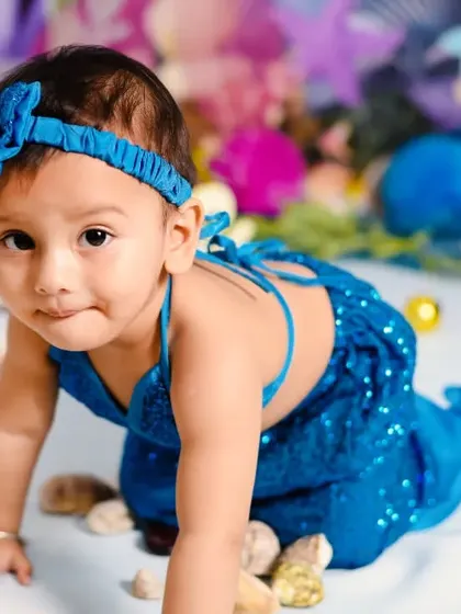 A close-up portrait from the mermaid-themed shoot, capturing her curious expression and the details of her sparkling blue costume and headband.