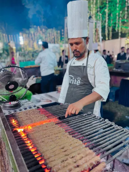 A chef carefully tends to long mutton seekh kebabs on the grill, ensuring they are cooked to perfection.