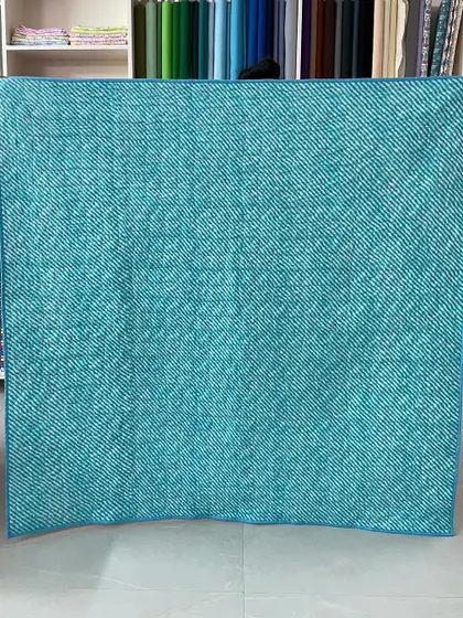 The back of a "Trip Around the World" quilt, featuring a solid teal fabric that highlights the quilting.
