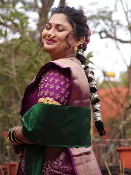 This side profile highlights the traditional Maharashtrian bridal hairstyle, adorned with intricate hair accessories, and the elegant drape of her saree and shawl.