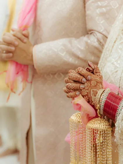 A close-up on the hands of the bride and groom during the Anand Karaj ceremony, symbolizing their union and shared prayers. A powerful detail shot.