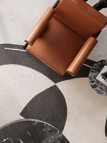An artistic flat-lay of materials and furniture, showing the leather of the armchair against the graphic pattern of the rug and the marble of the coffee table.
