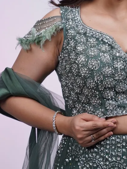 A close-up of the dark green lehenga's blouse. The combination of sequins and feather details on the shoulder adds a touch of modern glamour.