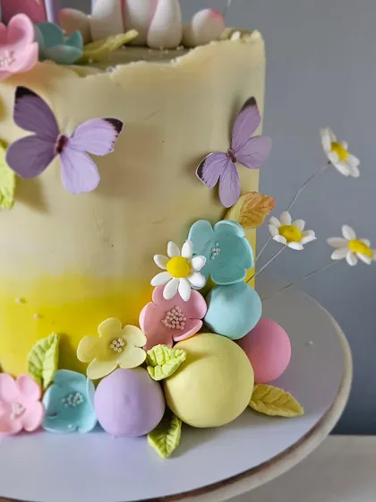 A detail shot of the side of the unicorn cake, showing the delicate, handcrafted sugar flowers and edible butterflies. Each element is carefully placed to build the enchanting garden theme.
