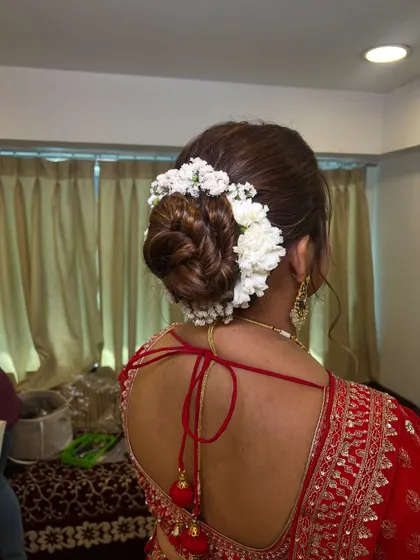 A clean and classic bridal bun wrapped in a string of fresh white flowers (gajra). This traditional hairstyle is elegant and perfectly complements a red lehenga.