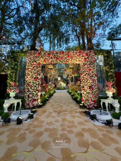A grand floral entrance arch for an outdoor wedding, made with a profusion of pink and red flowers, leading to a magical walkway.
