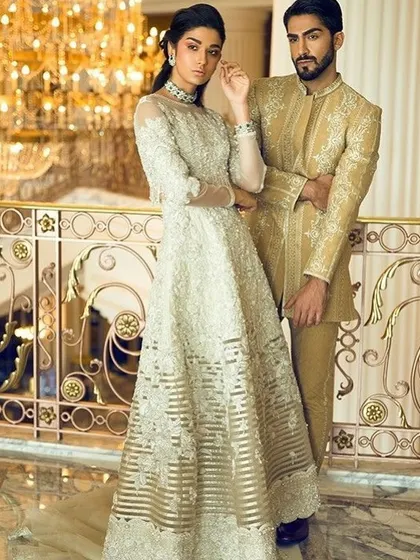 A vision of opulence, this couple is dressed in coordinated golden and off-white outfits. The groom's embroidered sherwani perfectly matches the bride's handcrafted gown, ideal for a lavish reception.