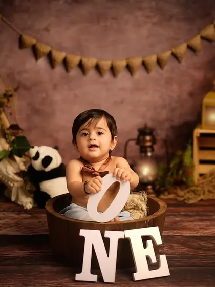 A happy boy in a tub, ready for his first birthday photos. The rustic, jungle-themed backdrop with stuffed animals creates a playful atmosphere for his milestone session.