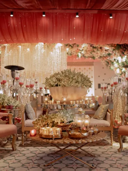 A grand seating area featuring a massive brass bowl filled with tuberoses. The warm lighting from the draped ceiling and candles creates a luxurious and inviting atmosphere.
