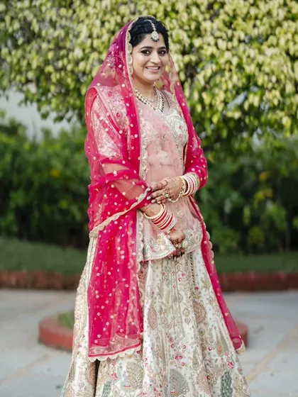 A full-length shot of the bride for her sunset wedding. The pastel lehenga is complemented by soft makeup and a pop of color from the pink dupatta.