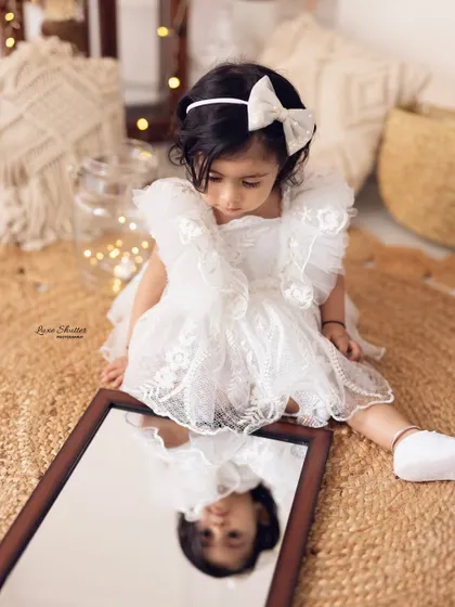 A creative and introspective moment, as the birthday girl looks at her own reflection in a mirror during her boho-themed first birthday shoot.