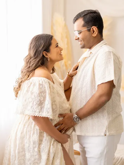 A playful and loving interaction between the parents-to-be. The mother-to-be adjusts her partner's shirt as they share a smile, a candid moment that shows their genuine connection during their maternity photoshoot.