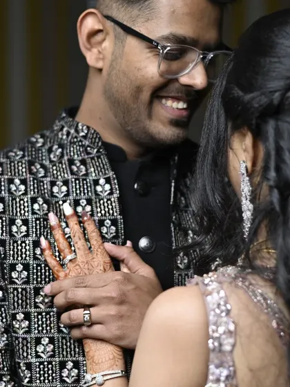 A close-up, tender moment between the couple at their engagement party, highlighting the bride's mehndi and the couple's rings.