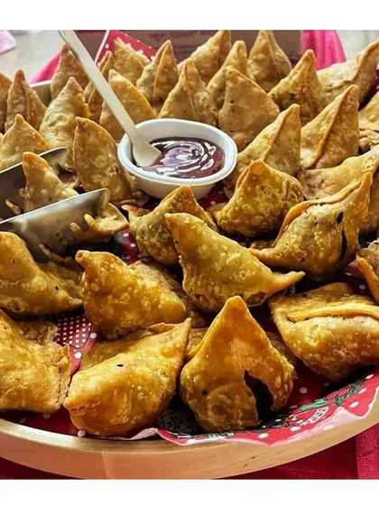 A platter of hot and crispy mini samosas served with a sweet and tangy dipping sauce, a classic Indian snack perfect for any occasion.