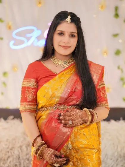 A radiant solo portrait of the mother-to-be at her baby shower. She is dressed in a stunning yellow and red saree, with beautiful henna on her hands, surrounded by festive decorations.