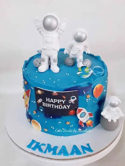 A beautiful space themed cake with astronaut figurines. The deep blue buttercream is decorated with planets and rockets for an interstellar adventure.